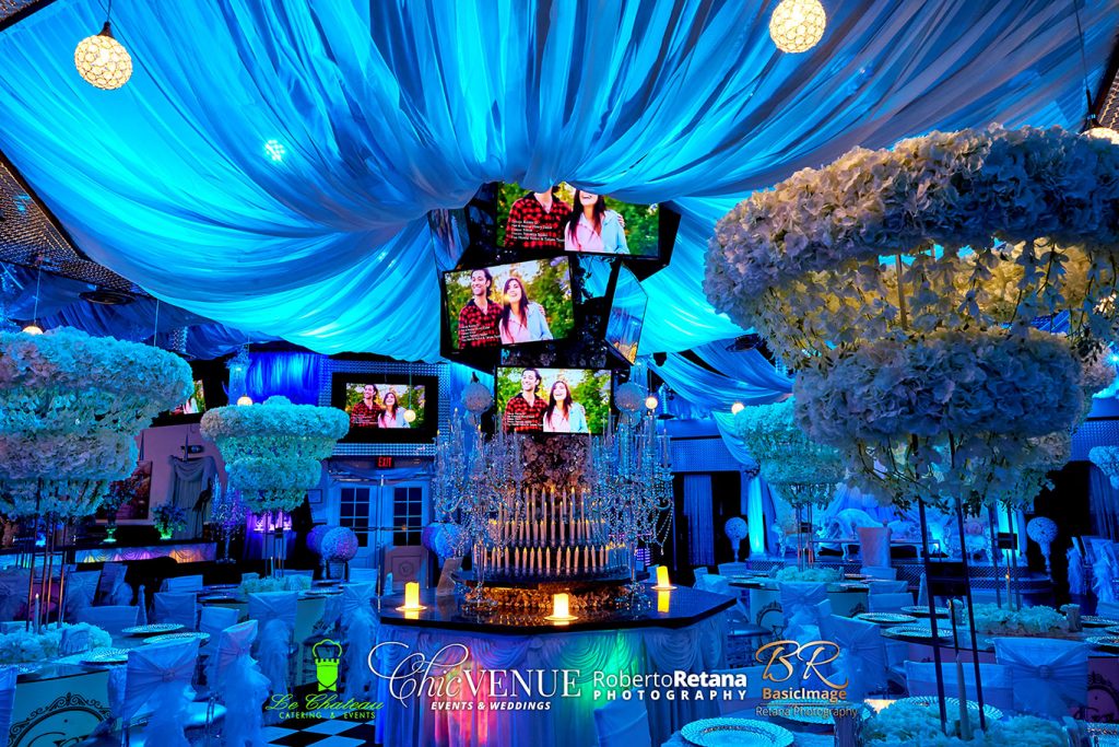 Blue-lit event room with floral decor and multiple video screens at Chic Venue
